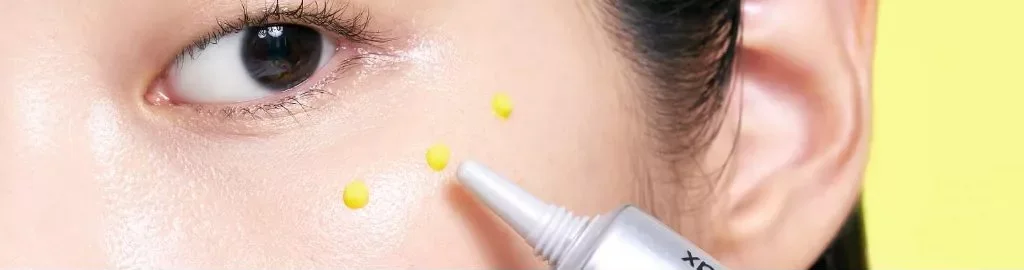 Imagem da marca: pequenos pontos do gel amarelo aplicados próximos à região dos olhos com a ponta do tubo
